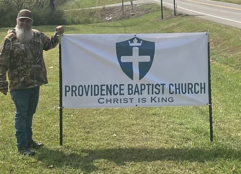 A church member standing beside the Providence Baptist Church banner, which reads “Christ is King.”